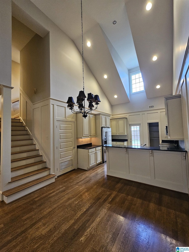 kitchen with stainless steel fridge with ice dispenser, dark countertops, dark wood-style flooring, a peninsula, and a notable chandelier