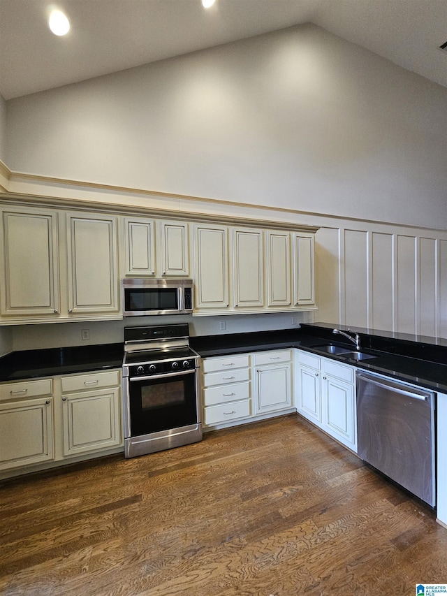 kitchen featuring cream cabinets, stainless steel appliances, a sink, dark wood-style floors, and dark countertops