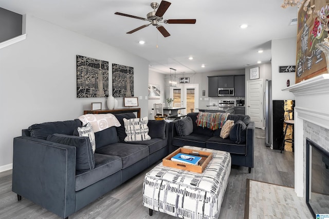 living area with light wood-style floors, recessed lighting, a fireplace, and ceiling fan with notable chandelier