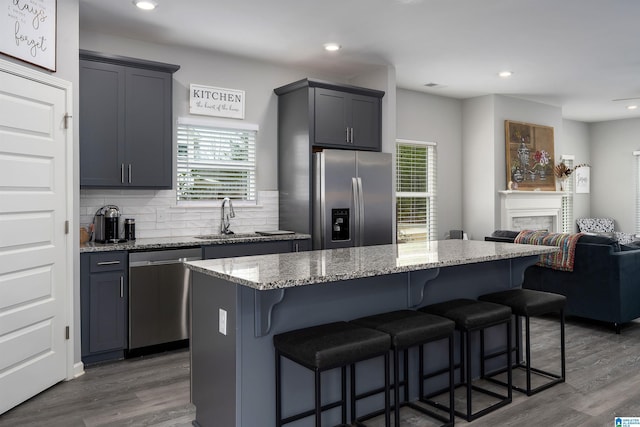 kitchen with stone countertops, stainless steel appliances, a sink, a kitchen breakfast bar, and dark wood-style floors