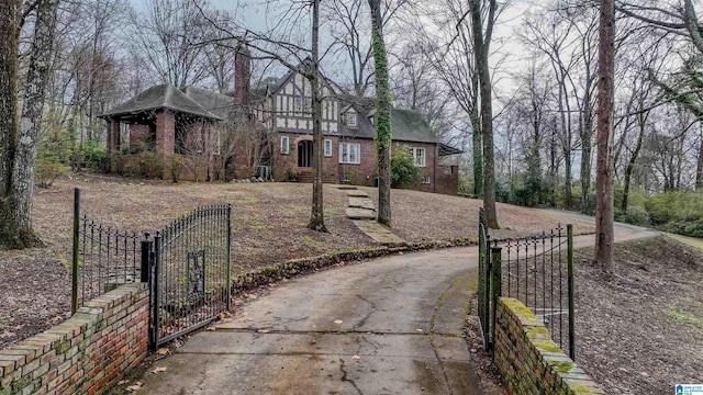 tudor home featuring a gate, brick siding, and fence