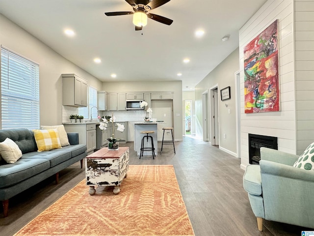 living room featuring a large fireplace, baseboards, ceiling fan, light wood-style floors, and recessed lighting