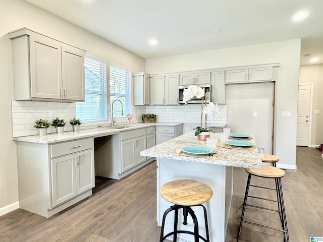 kitchen with light wood finished floors, decorative backsplash, stainless steel microwave, a kitchen breakfast bar, and a sink