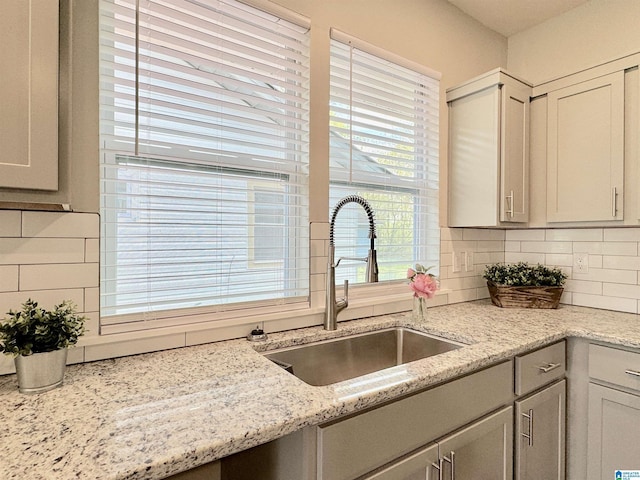 kitchen with tasteful backsplash, gray cabinets, a sink, and light stone counters