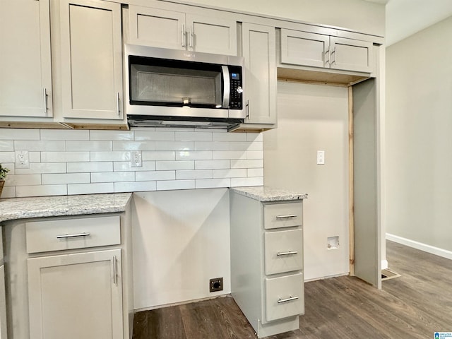 kitchen with tasteful backsplash, stainless steel microwave, dark wood finished floors, and light stone countertops