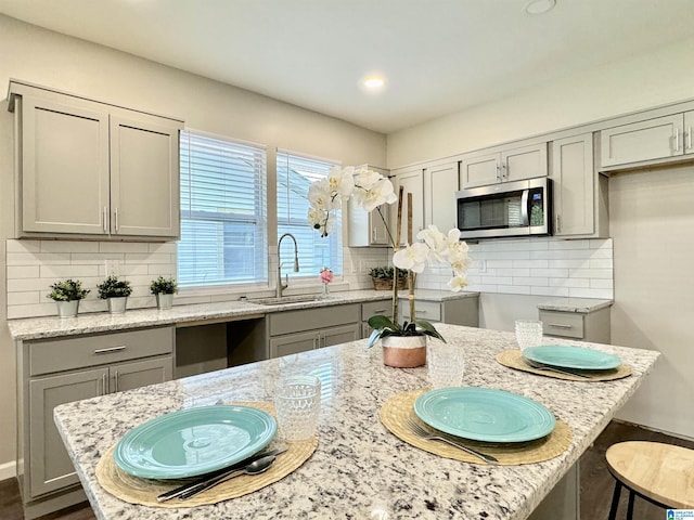 kitchen with stainless steel microwave, a sink, gray cabinetry, and light stone countertops