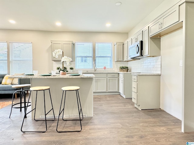 kitchen featuring a breakfast bar, a kitchen island, light wood-style floors, backsplash, and stainless steel microwave