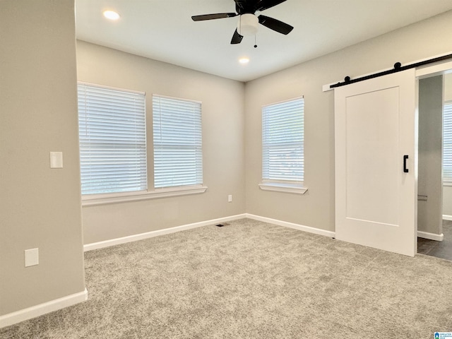 carpeted empty room with ceiling fan, a barn door, recessed lighting, visible vents, and baseboards