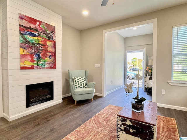 living area with a large fireplace, plenty of natural light, wood finished floors, and baseboards