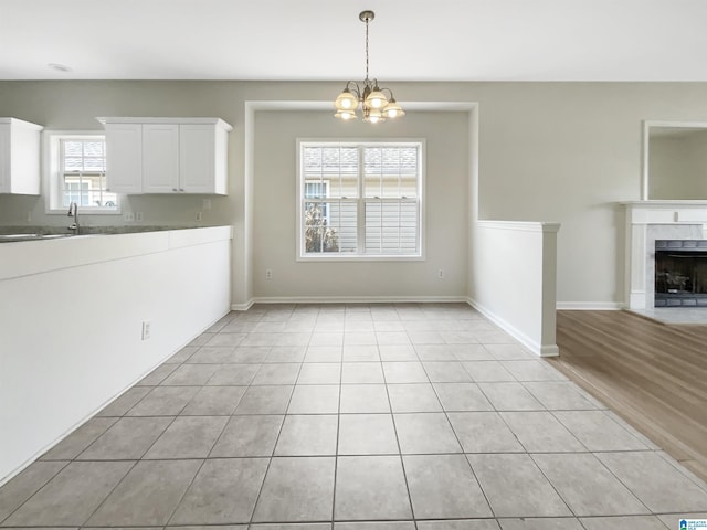 unfurnished dining area with light tile patterned floors, a premium fireplace, baseboards, and a notable chandelier