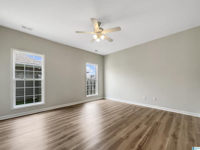 empty room with visible vents, wood finished floors, a ceiling fan, and baseboards