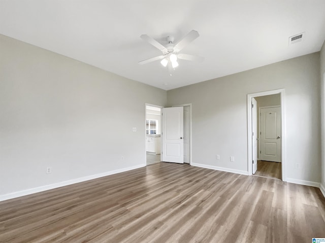 unfurnished room with a ceiling fan, wood finished floors, visible vents, and baseboards