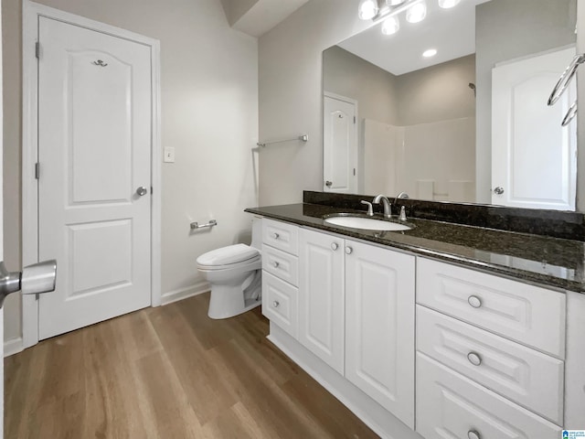 full bathroom featuring toilet, wood finished floors, vanity, baseboards, and a shower