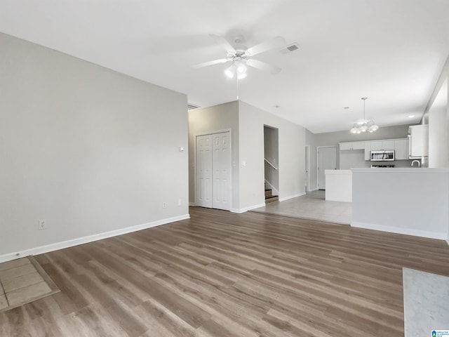 unfurnished living room with wood finished floors, visible vents, baseboards, and stairs