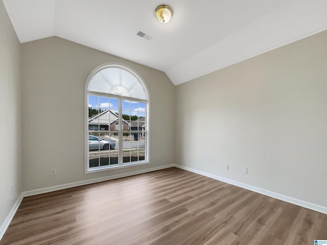 empty room featuring vaulted ceiling, wood finished floors, visible vents, and baseboards