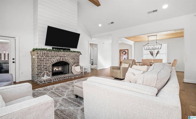 living room with visible vents, a brick fireplace, high vaulted ceiling, and wood finished floors