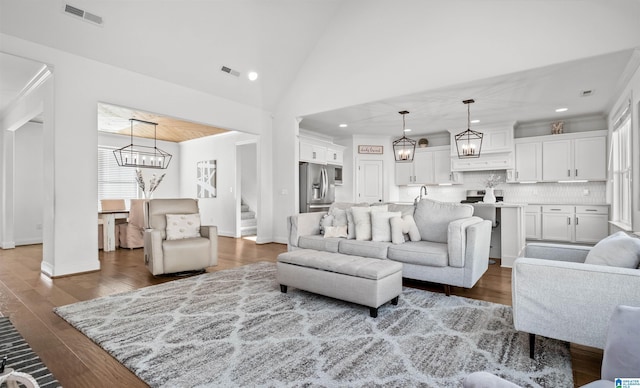 living area featuring a chandelier, stairway, visible vents, and wood finished floors