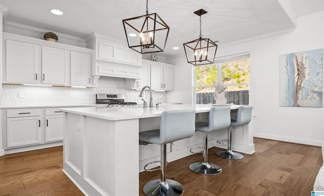 kitchen with tasteful backsplash, stainless steel range with gas cooktop, a kitchen island with sink, and ornamental molding