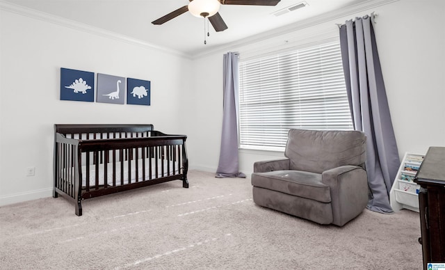 carpeted bedroom featuring baseboards, visible vents, ceiling fan, a crib, and crown molding