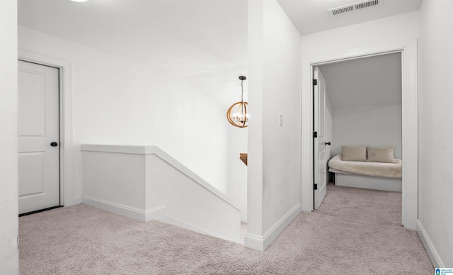 hall with an upstairs landing, visible vents, an inviting chandelier, and carpet