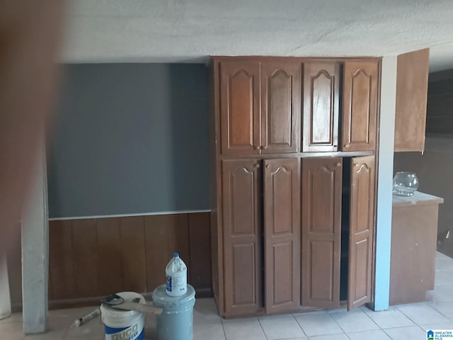 interior space featuring a wainscoted wall, light countertops, a textured ceiling, and light tile patterned flooring