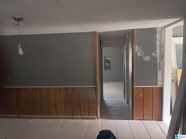 corridor with wood walls, a textured ceiling, and wainscoting