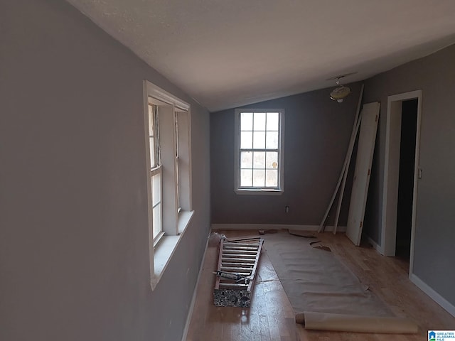 spare room with lofted ceiling, light wood-style flooring, and baseboards