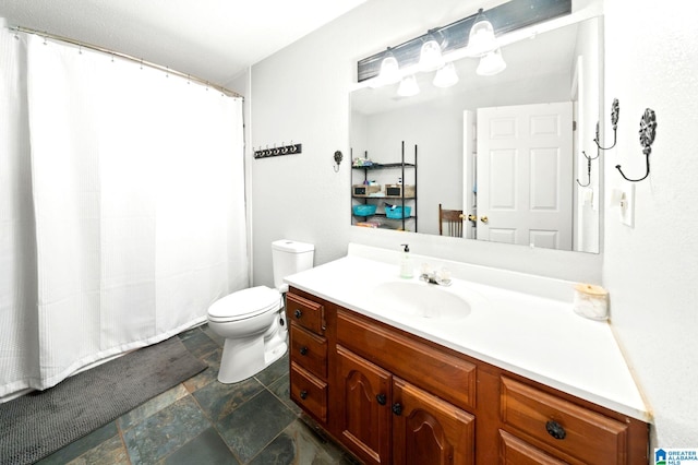 bathroom featuring stone finish flooring, a shower with shower curtain, vanity, and toilet