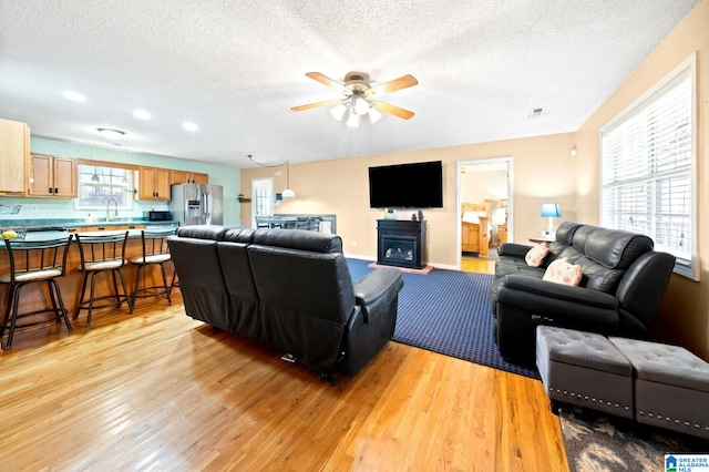 living area with light wood-style flooring, baseboards, ceiling fan, and a textured ceiling