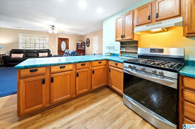 kitchen featuring stainless steel gas range oven, light wood-style floors, open floor plan, a peninsula, and under cabinet range hood