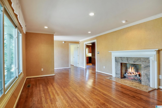 unfurnished living room with baseboards, a premium fireplace, wood finished floors, crown molding, and recessed lighting