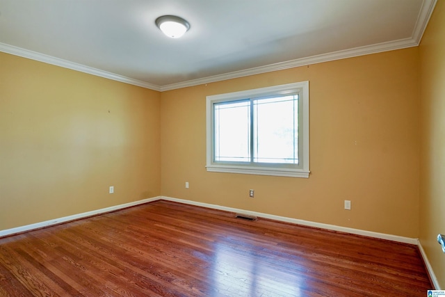 spare room featuring ornamental molding, visible vents, baseboards, and wood finished floors