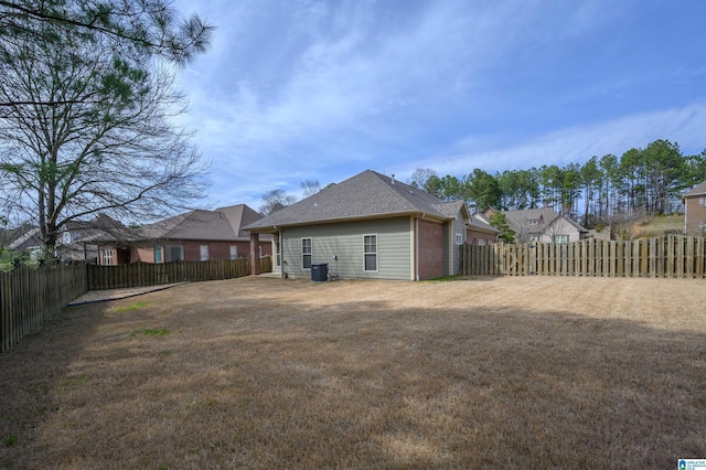 back of house featuring a fenced backyard, central AC, a lawn, and brick siding