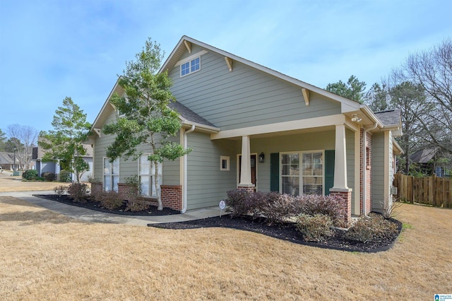 view of front of house with brick siding, a front lawn, a shingled roof, and fence