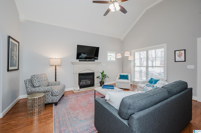 living area with wood finished floors, a ceiling fan, baseboards, ornamental molding, and a glass covered fireplace