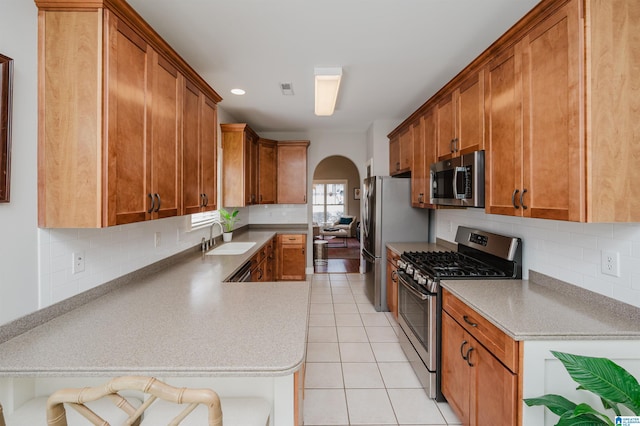 kitchen featuring arched walkways, brown cabinetry, appliances with stainless steel finishes, a sink, and light tile patterned flooring