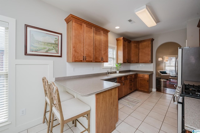 kitchen with arched walkways, brown cabinets, freestanding refrigerator, a peninsula, and gas stove