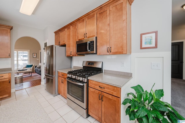 kitchen with light tile patterned floors, arched walkways, stainless steel appliances, and decorative backsplash