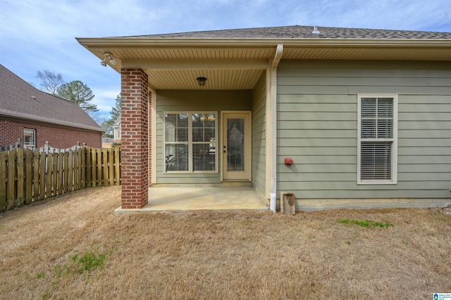 rear view of property with roof with shingles, brick siding, fence, and a patio