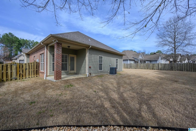 back of property with central air condition unit, a yard, a fenced backyard, and brick siding