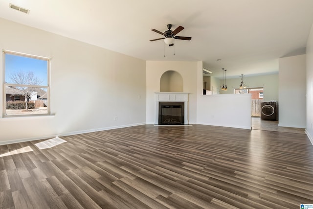 unfurnished living room with dark wood finished floors, visible vents, washer / dryer, and a fireplace with flush hearth