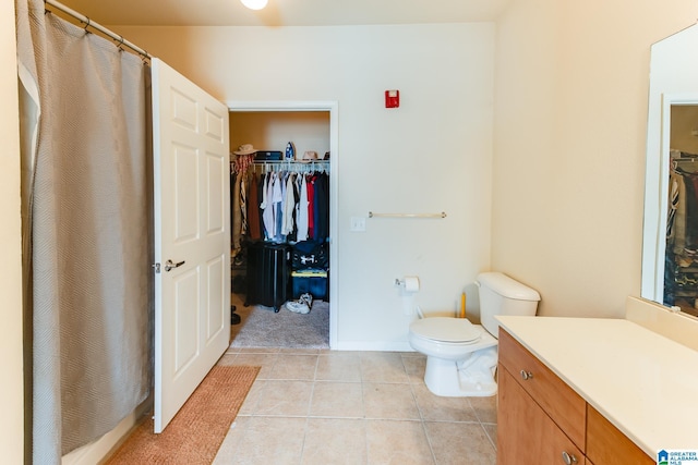 full bath with baseboards, toilet, tile patterned flooring, a walk in closet, and vanity