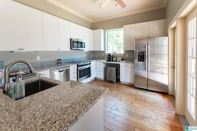 kitchen with stainless steel appliances, a sink, light wood-type flooring, light stone countertops, and crown molding