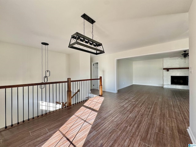 interior space with ceiling fan, baseboards, wood finished floors, and a stone fireplace