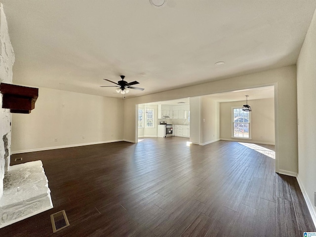 unfurnished living room featuring dark wood-type flooring, visible vents, ceiling fan, and a stone fireplace