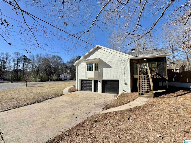 view of property exterior with brick siding, concrete driveway, stairway, an attached garage, and a sunroom