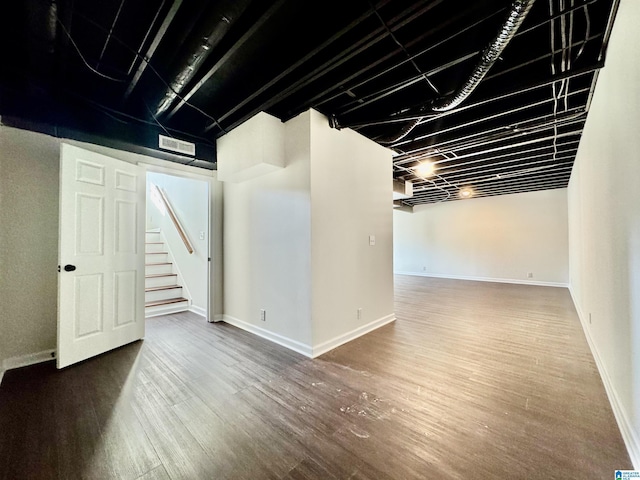 finished below grade area with visible vents, stairway, baseboards, and wood finished floors