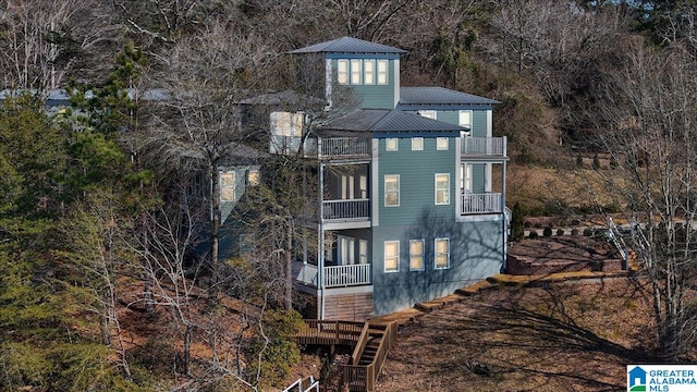 rear view of property featuring a balcony, a standing seam roof, stairway, and metal roof