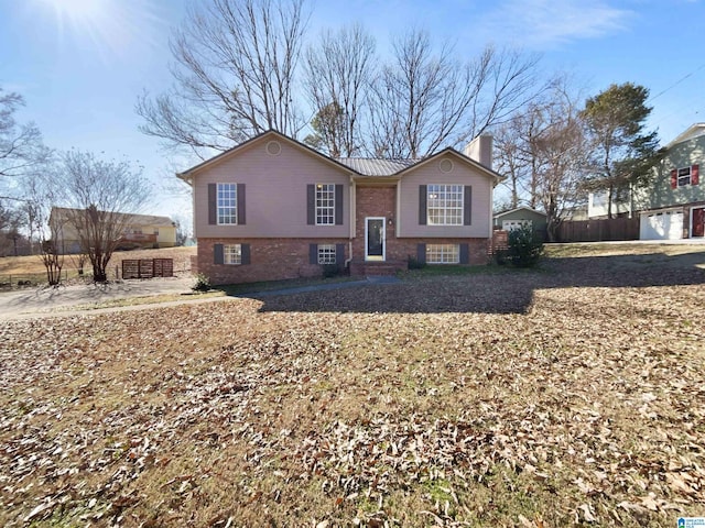 split foyer home featuring brick siding, a chimney, and fence