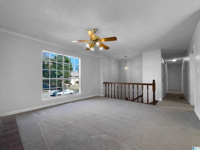 carpeted spare room with baseboards, visible vents, ceiling fan, crown molding, and a textured ceiling